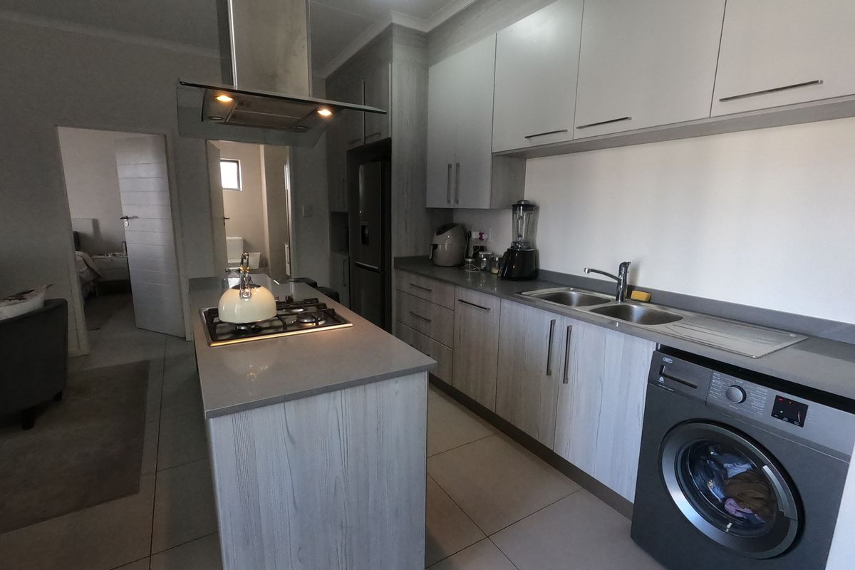 Modern kitchen featuring a central island with gas hob, extractor fan, ample cabinetry, double sink, and integrated laundry space with tiled flooring.