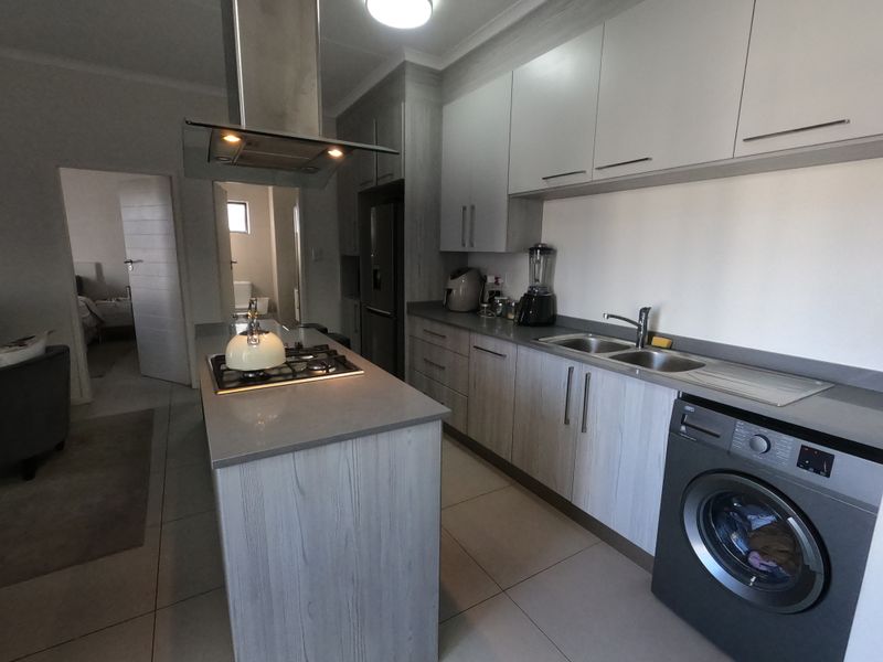 Modern kitchen featuring a central island with gas hob, extractor fan, ample cabinetry, double sink, and integrated laundry space with tiled flooring.