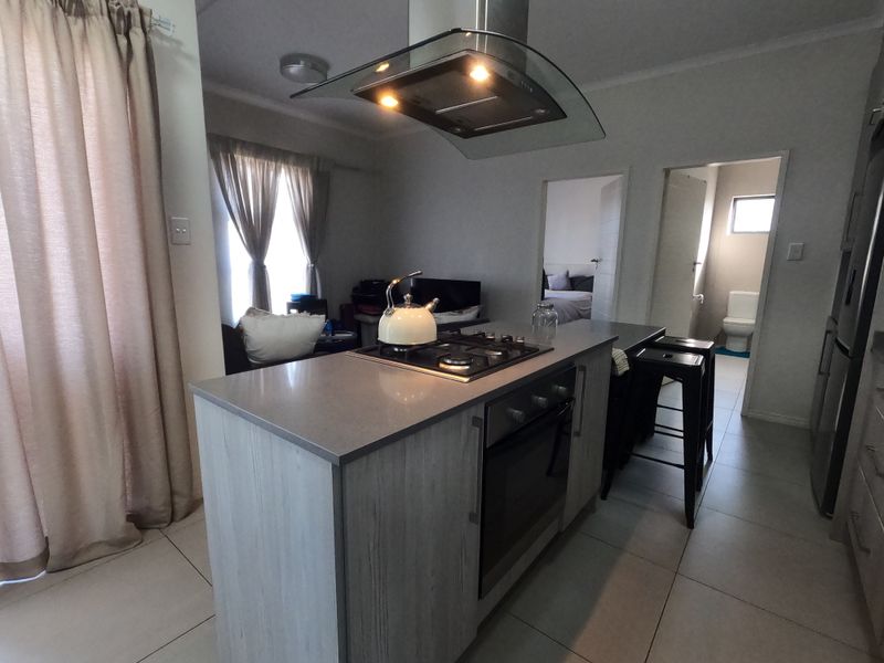 Open-plan kitchen featuring a central island with a gas hob, built-in oven, and modern extractor fan, finished with neutral floor tiles.