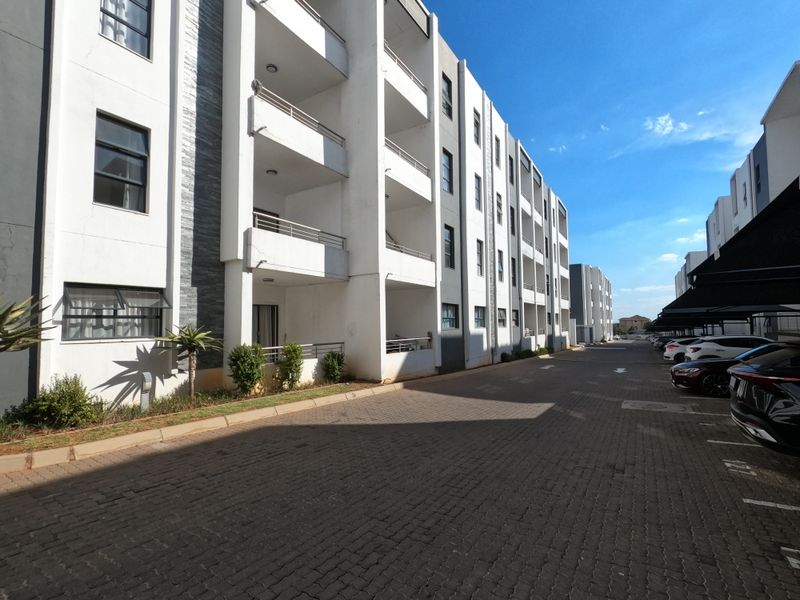 Exterior view of a modern apartment complex featuring multi-level balconies, stone-accented facade, and paved driveway with covered parking bays.