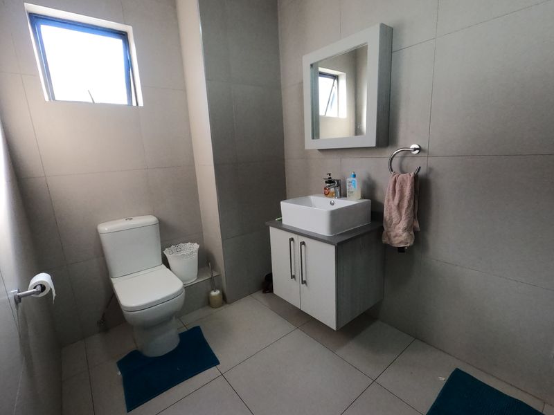 A modern bathroom featuring a wall-mounted vanity with a vessel sink, a toilet, and neutral wall tiling.
