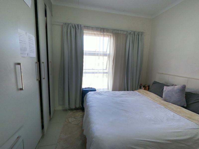 A functional bedroom featuring built-in cupboards, tiled flooring, and a window with curtain rails, providing a neutral base for personalization.