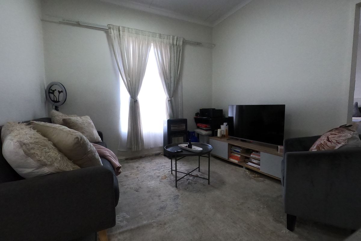 A living room space featuring a window with curtain rails and exposed, worn flooring in need of refurbishment.