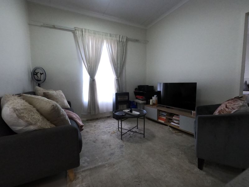 A living room space featuring a window with curtain rails and exposed, worn flooring in need of refurbishment.