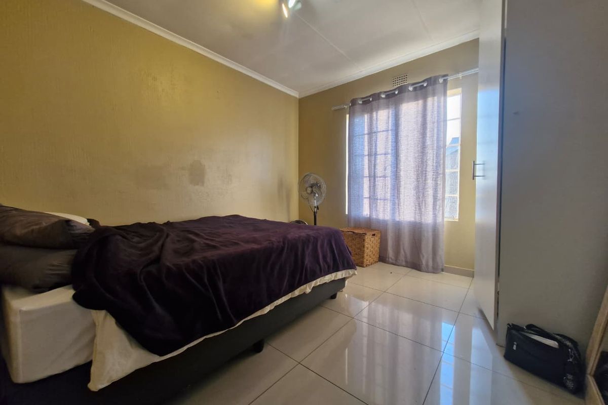 A bedroom featuring tiled flooring, a built-in wardrobe, and a window with curtains, providing a functional living space.