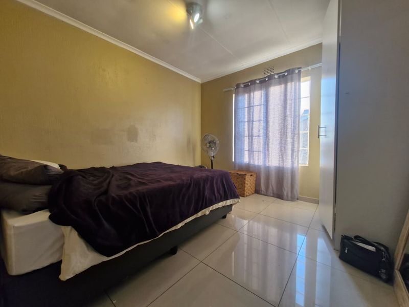 A bedroom featuring tiled flooring, a built-in wardrobe, and a window with curtains, providing a functional living space.