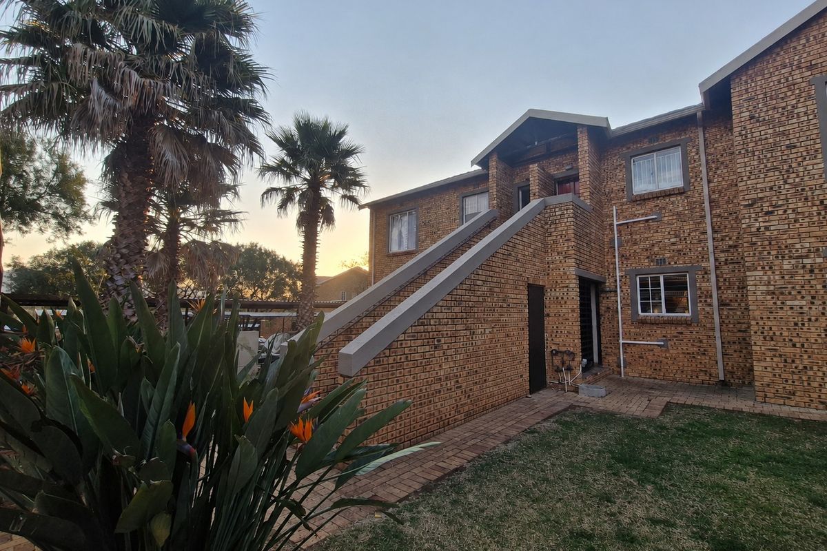 Rear view of a face brick apartment building featuring an external staircase, paved pathways, and established garden landscaping.