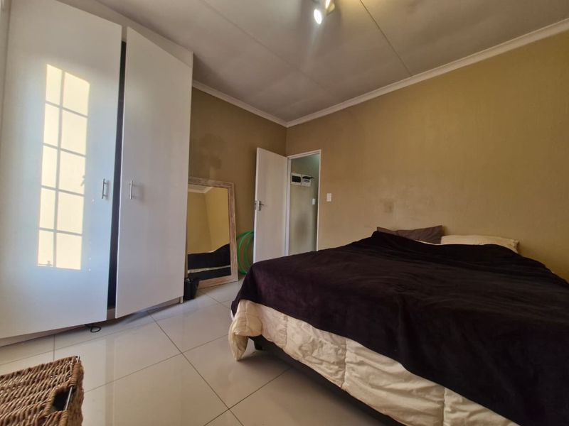 A bedroom featuring tiled flooring, built-in wardrobes, and neutral wall tones, offering a functional space with potential for cosmetic updates.