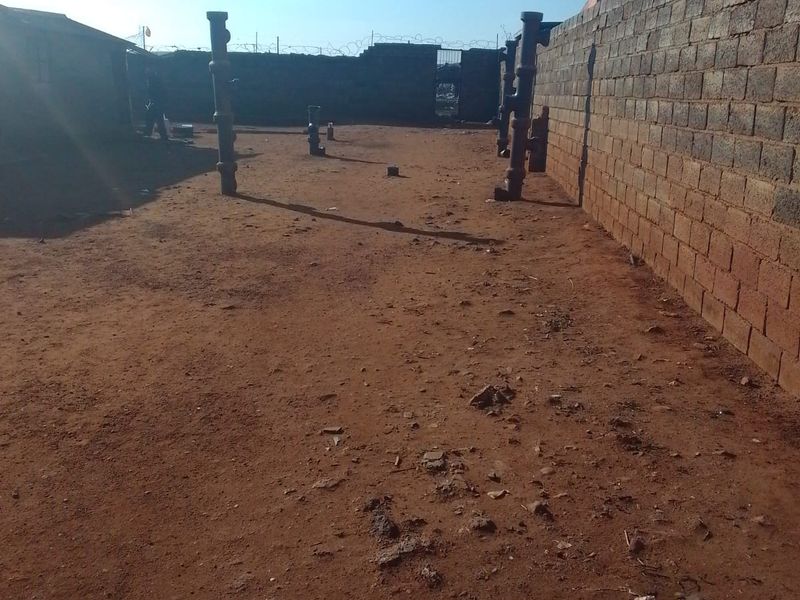 An expansive, undeveloped rear yard area enclosed by perimeter brick walls with security razor wire and existing structural support columns.