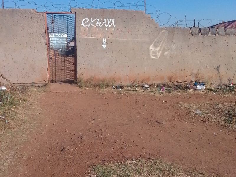 Front view of the property featuring a perimeter wall with razor wire and a metal access gate.