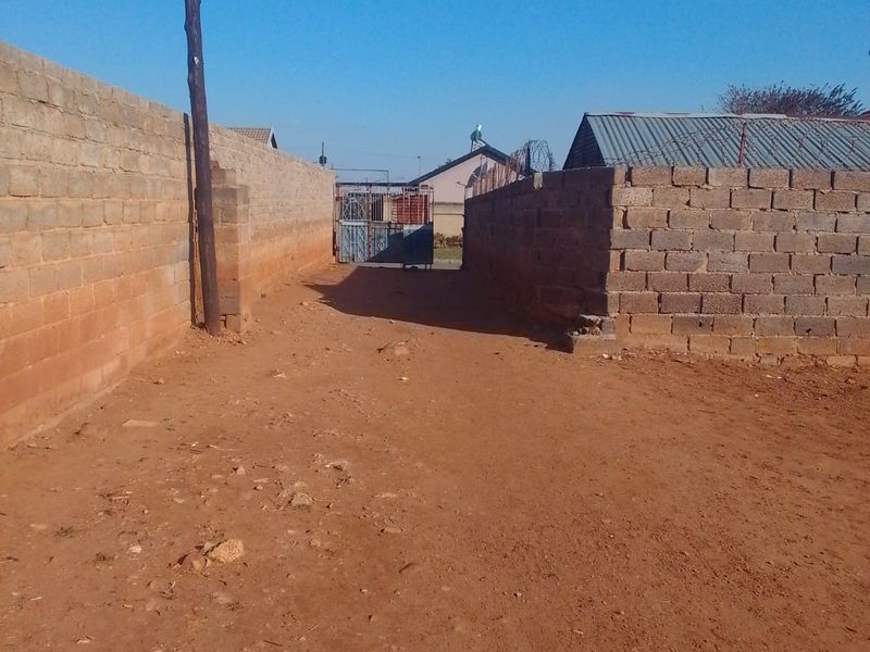 A view of the property entrance featuring a dirt driveway enclosed by unfinished concrete block perimeter walls and a metal gate.
