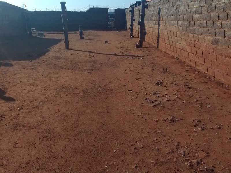 A large, undeveloped outdoor space enclosed by perimeter brick walls with security fencing, offering a blank canvas for landscaping or future development.