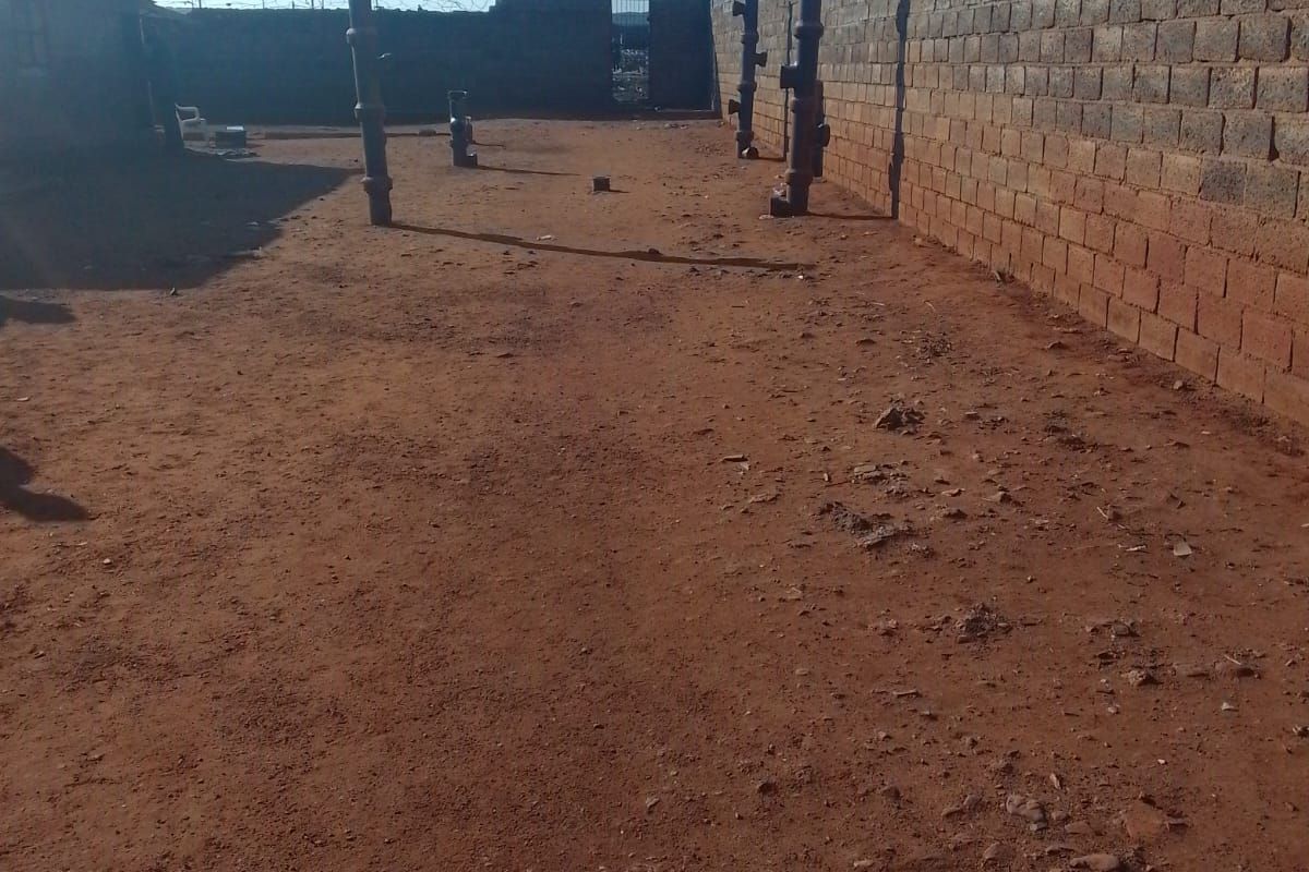 A large, undeveloped outdoor space enclosed by perimeter brick walls with security fencing, offering a blank canvas for landscaping or future development.
