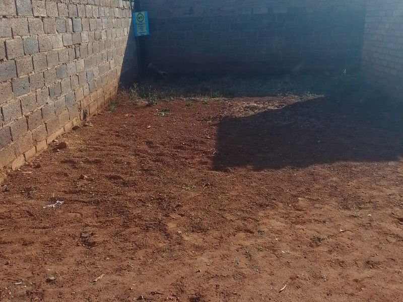 A rear yard area enclosed by brick perimeter walls with razor wire, featuring an unlandscaped dirt surface ready for development or garden design.