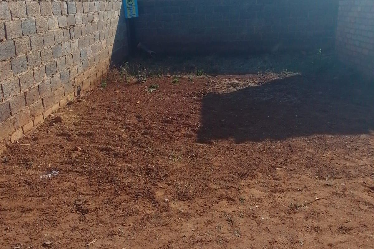 A rear yard area enclosed by brick perimeter walls with razor wire, featuring an unlandscaped dirt surface ready for development or garden design.