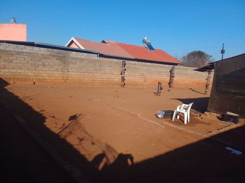 A spacious rear yard featuring a perimeter wall, tiled roof structure, and solar water heating system, offering potential for landscaping and outdoor development.