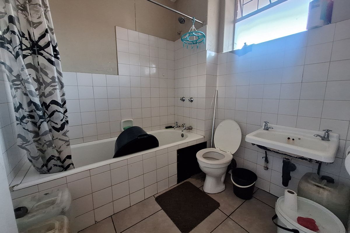 A dated bathroom featuring a bathtub, wall-mounted basin, and toilet with tiled finishes, requiring renovation to modernize the space.