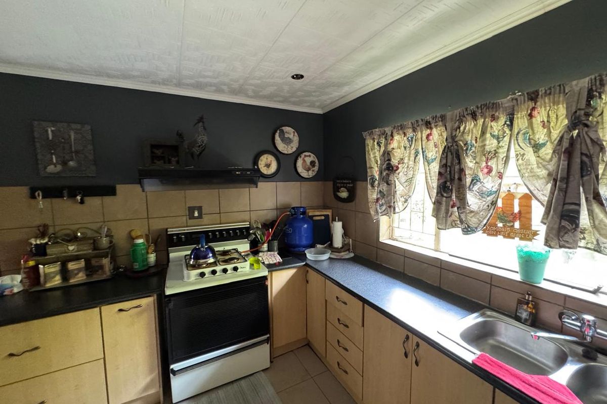 A functional kitchen featuring light wood cabinetry, dark countertops, a built-in stove with extractor fan, and a double stainless steel sink.