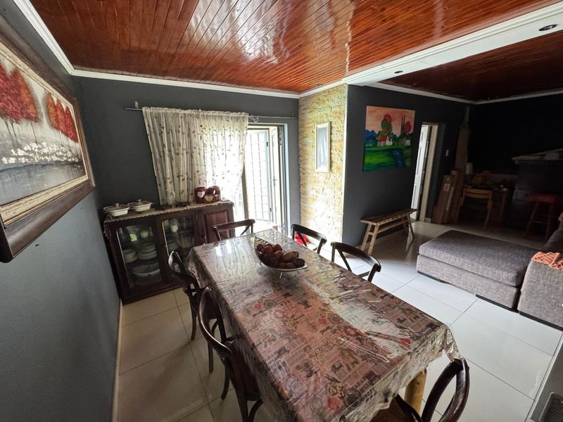 Open plan dining and living area featuring tiled flooring, a timber-clad ceiling, and a stone-cladding feature wall with access to the exterior.