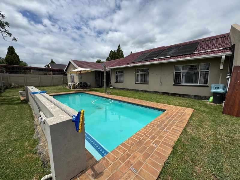 Rear garden featuring a swimming pool with brick coping, solar heating panels on the roof, and a lawn area.