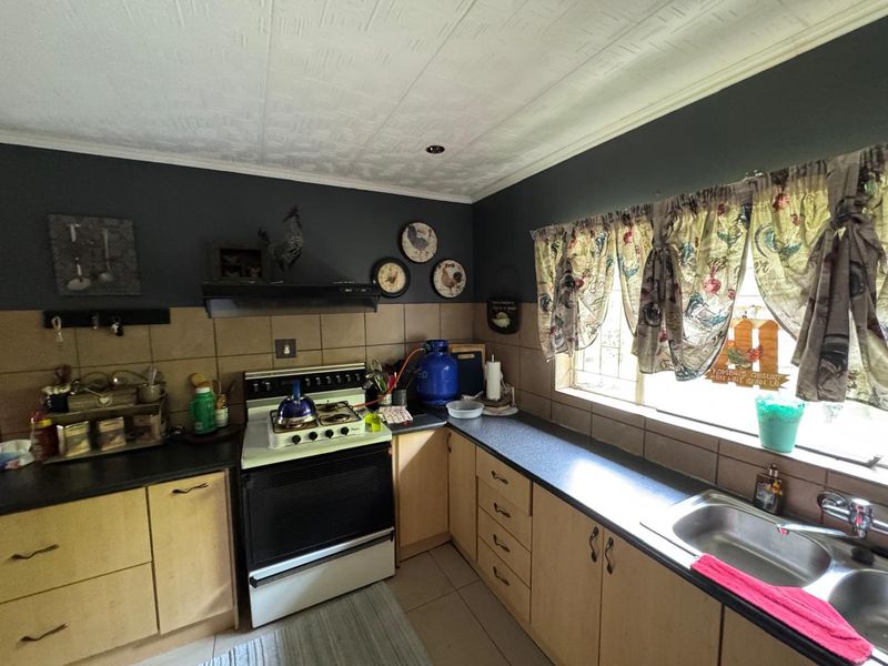 A functional kitchen featuring light wood cabinetry, dark countertops, a built-in stove with extractor fan, and a double stainless steel sink.
