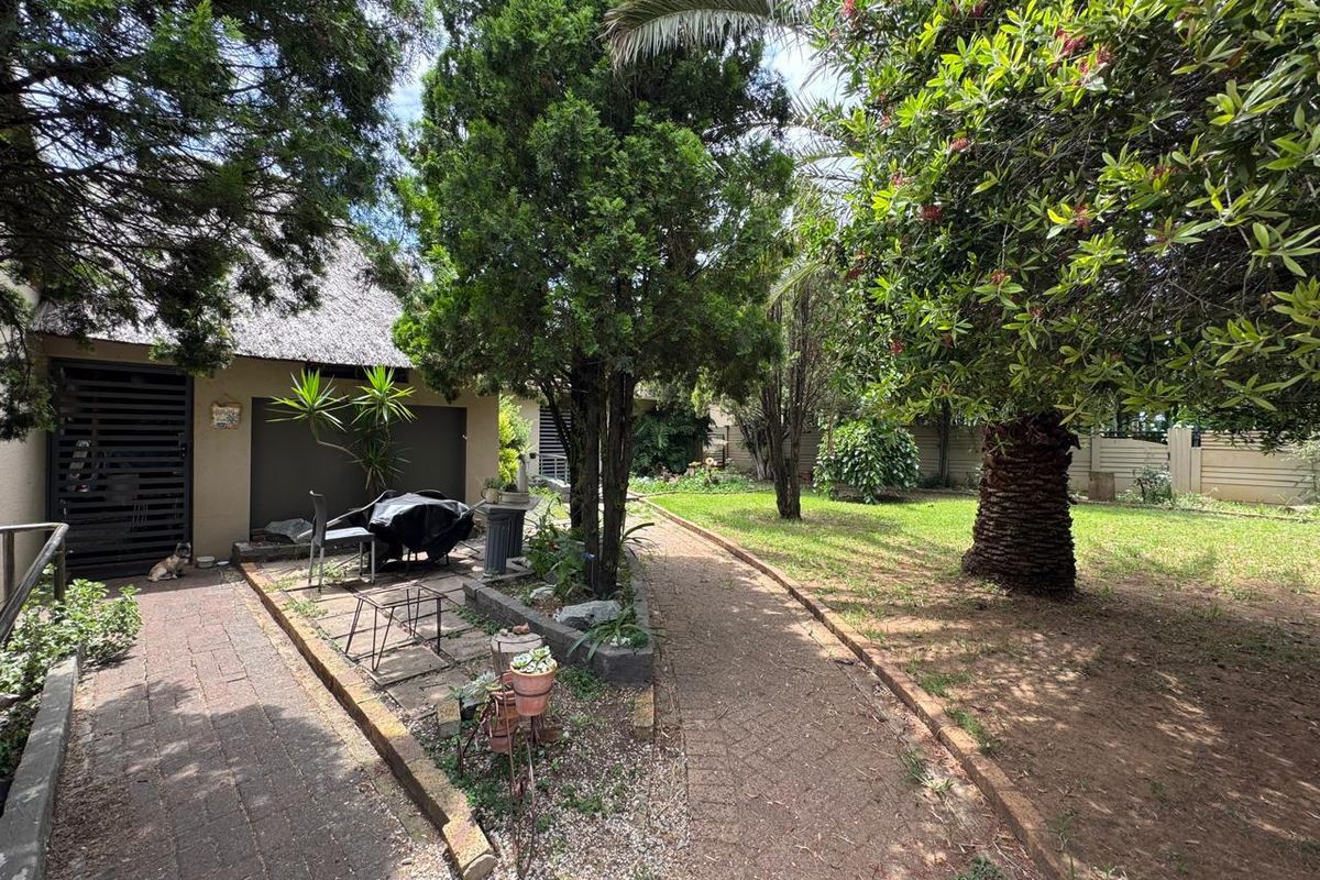 A spacious rear garden featuring mature trees, a paved walkway, and a covered patio area adjacent to the main dwelling.