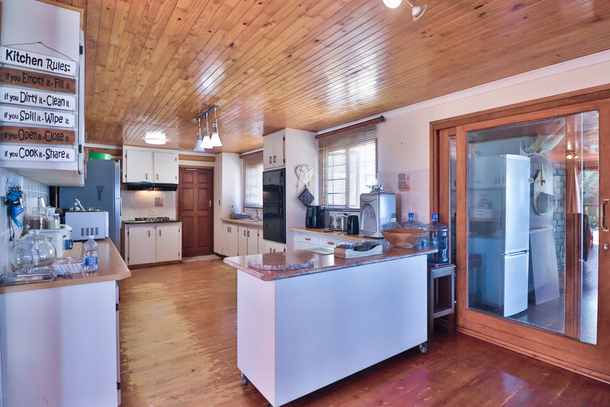 A dated kitchen featuring timber tongue and groove ceilings, timber flooring, built-in cabinetry, and a central island, offering potential for modernization.