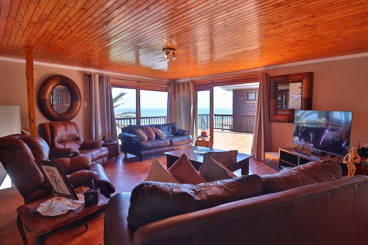 Spacious living room featuring warm timber tongue and groove ceilings, timber flooring, and large sliding glass doors opening onto a balcony with ocean views.