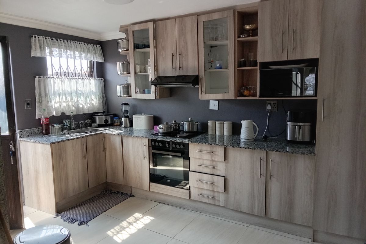 A functional kitchen featuring light wood-finish cabinetry, granite countertops, built-in oven, hob, and extractor fan, complemented by tiled flooring and natural light.