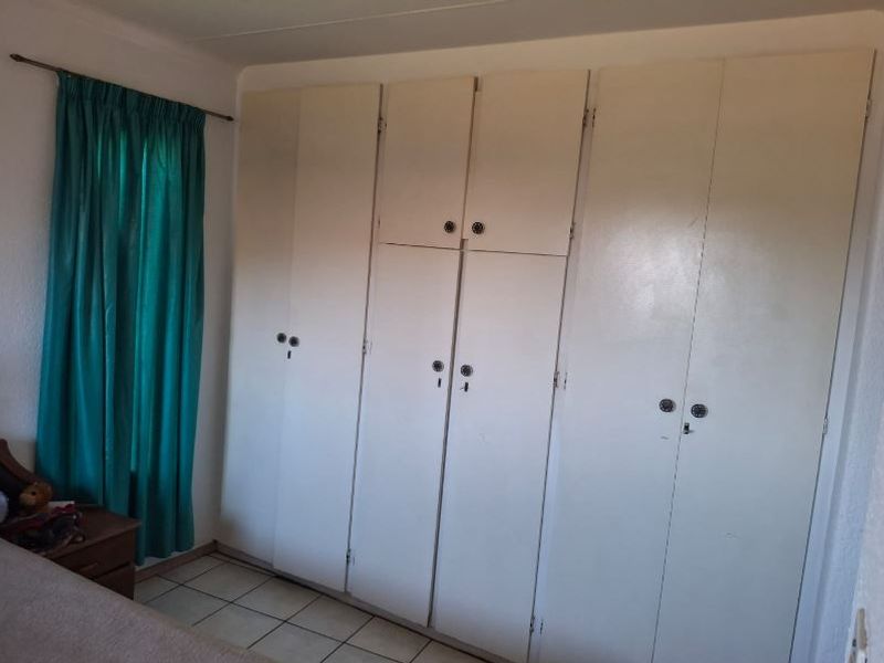 A bedroom featuring built-in cupboards with a dated finish and tiled flooring.