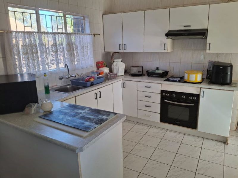 Functional kitchen featuring white cabinetry, laminate countertops, built-in oven, electric hob, extractor fan, and tiled splashbacks with tiled flooring.