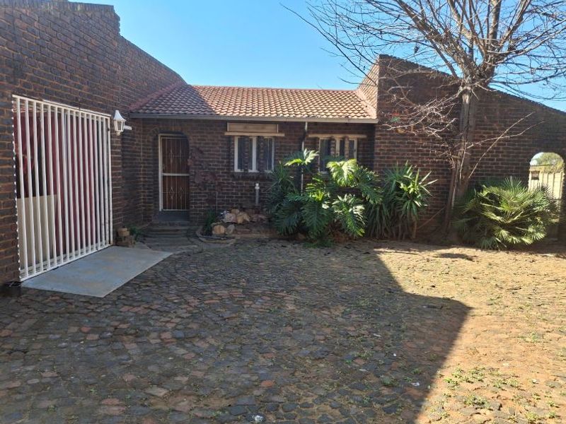 Front exterior view of a face brick house featuring a tiled roof, security gate, and a cobblestone driveway.