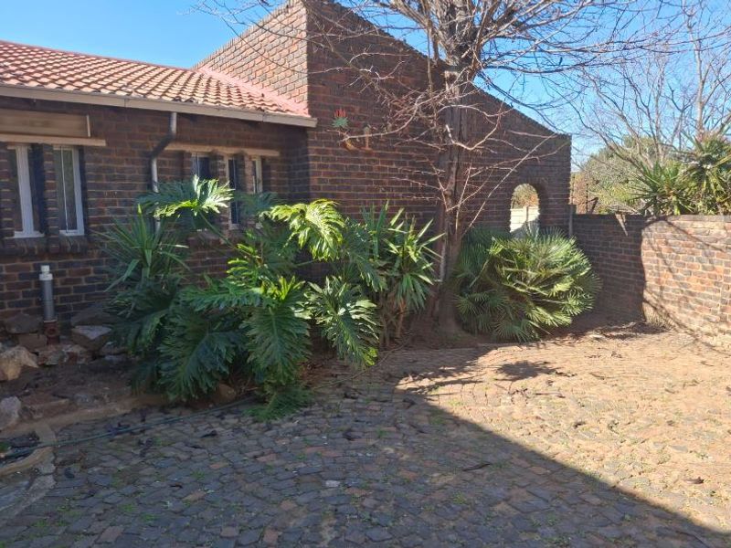 A rear exterior view of a face brick house featuring a tiled roof, cobblestone paving, and a brick boundary wall with an arched gate.