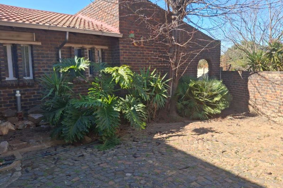 A rear exterior view of a face brick house featuring a tiled roof, cobblestone paving, and a brick boundary wall with an arched gate.