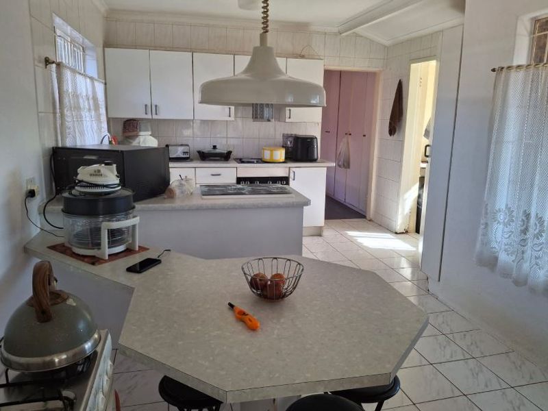 A functional kitchen featuring white cabinetry, laminate countertops, tiled flooring, and a central breakfast bar area, offering potential for modern updates.