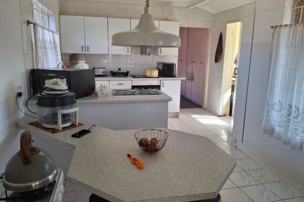 A functional kitchen featuring white cabinetry, laminate countertops, tiled flooring, and a central breakfast bar area, offering potential for modern updates.