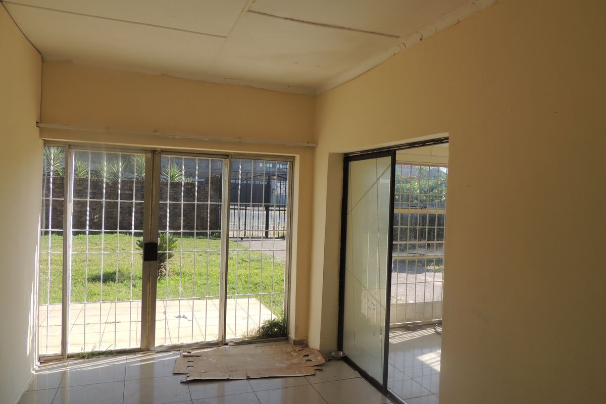 An empty living area featuring tiled flooring, sliding glass doors with security gates, and direct access to the outdoor garden space.