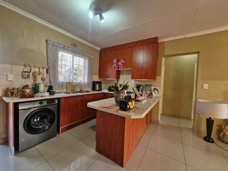 A functional kitchen featuring wood-look cabinetry, laminate countertops, tiled flooring, and an integrated washing machine space.