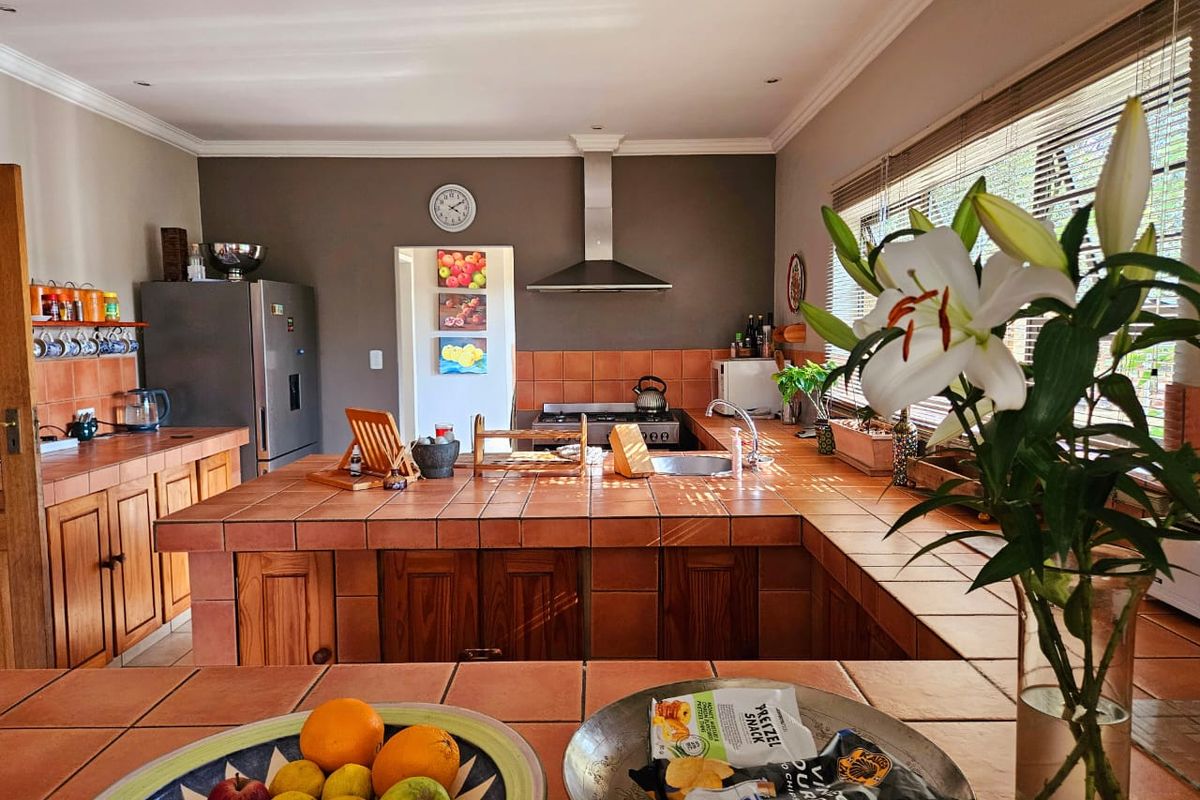 A functional kitchen featuring tiled countertops, wooden cabinetry, a stainless steel extractor fan, and a built-in gas hob with ample workspace.
