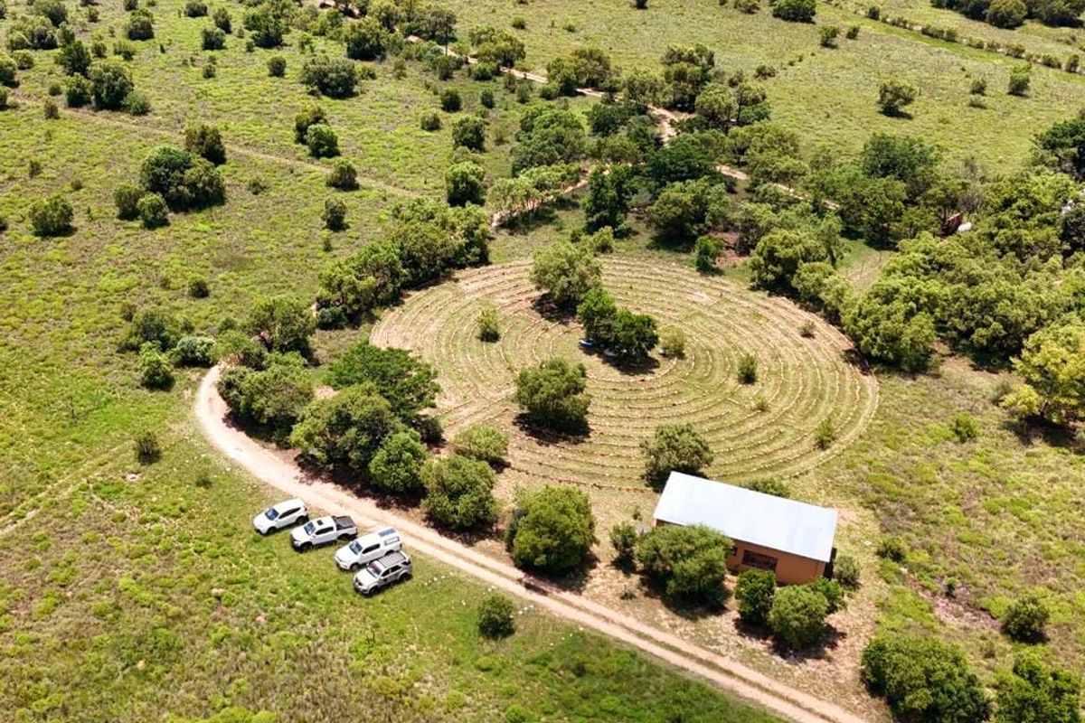 Aerial view of a rural property featuring a metal-roofed building, a circular landscaped garden, and a dirt access road.