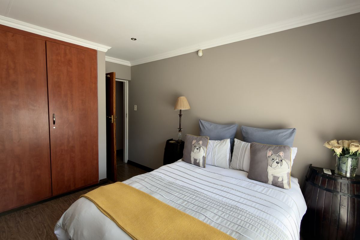 A well-maintained bedroom featuring built-in wooden cupboards, laminate flooring, and neutral wall tones, providing a comfortable and functional living space.