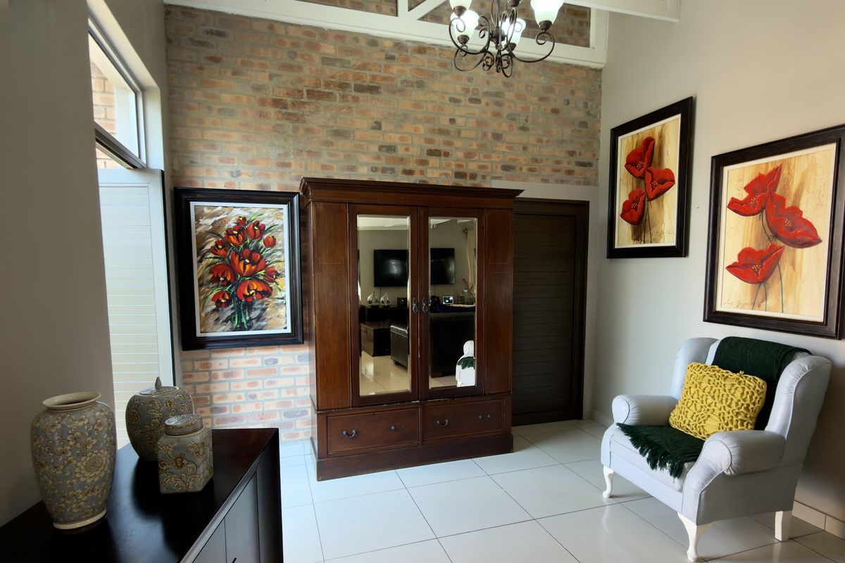 A living area featuring an exposed brick feature wall, vaulted ceilings with a chandelier, and neutral tiled flooring.