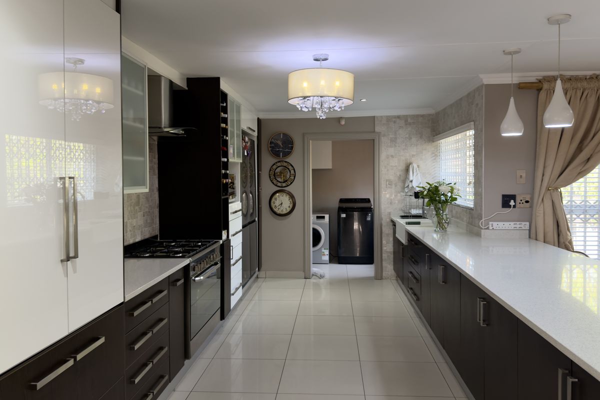 Modern kitchen featuring high-gloss cabinetry, quartz countertops, gas cooktop, built-in oven, and elegant pendant lighting, with an adjacent laundry area.