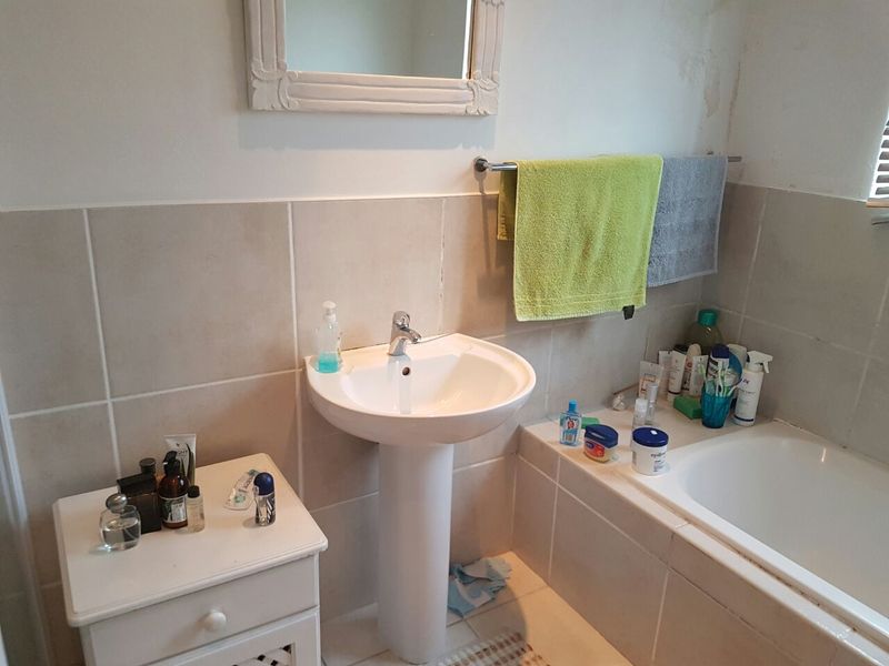 A functional bathroom featuring a pedestal basin, built-in bathtub, and tiled splashback, showing some signs of wear on the wall surface.