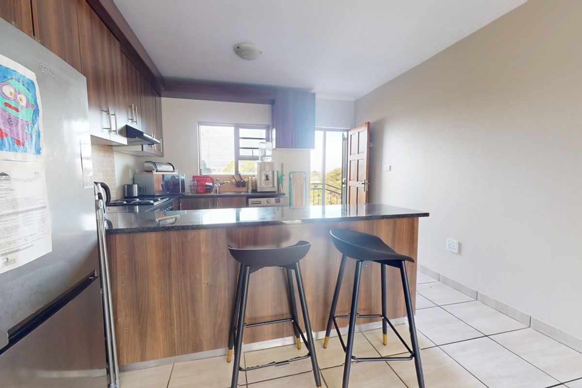 A functional kitchen featuring wood veneer cabinetry, granite countertops, a breakfast bar, and tiled flooring, with direct access to an outdoor area.
