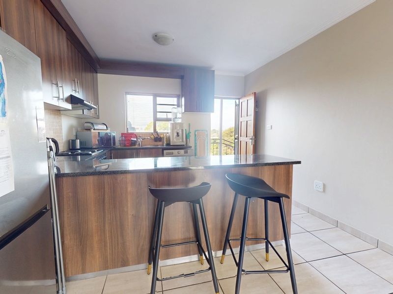 A functional kitchen featuring wood veneer cabinetry, granite countertops, a breakfast bar, and tiled flooring, with direct access to an outdoor area.
