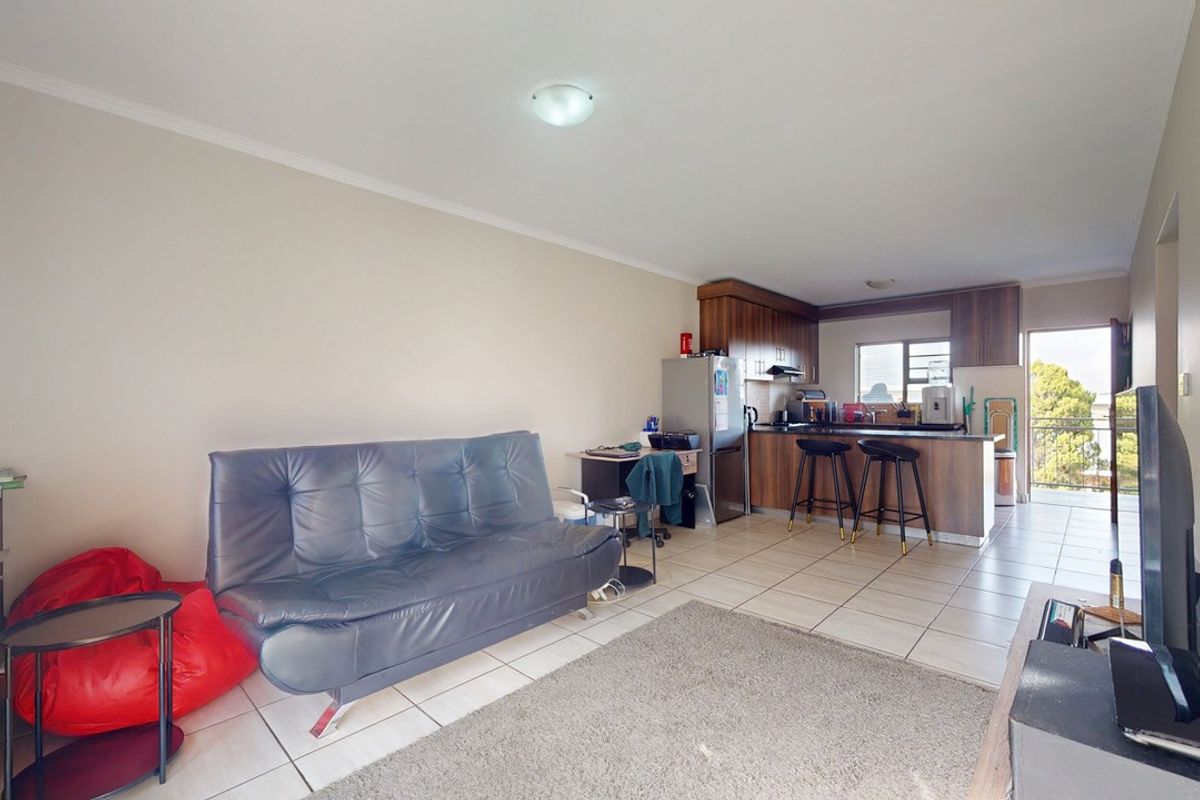 Open-plan living area featuring a kitchen with built-in cabinetry and a breakfast counter, flowing into a lounge space with tiled flooring.