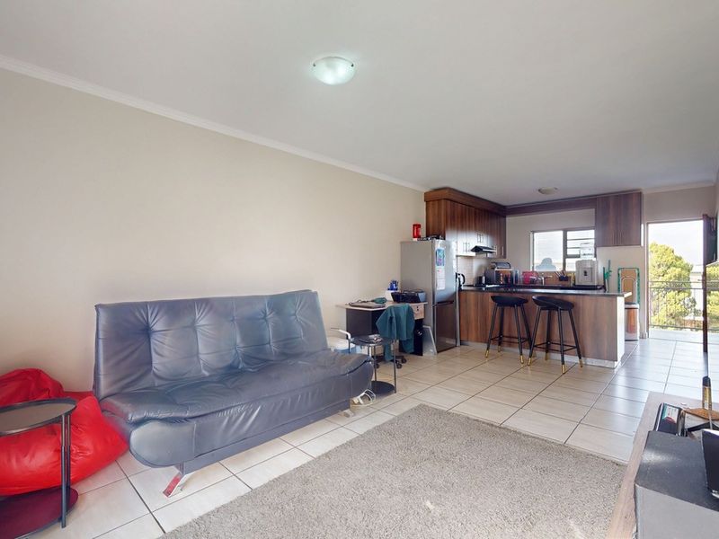 Open-plan living area featuring a kitchen with built-in cabinetry and a breakfast counter, flowing into a lounge space with tiled flooring.