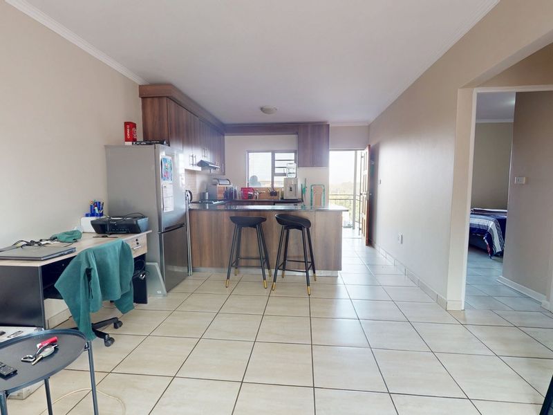 Open-plan kitchen and living area featuring tiled flooring, wooden cabinetry, and a breakfast bar island, leading to an outdoor balcony.