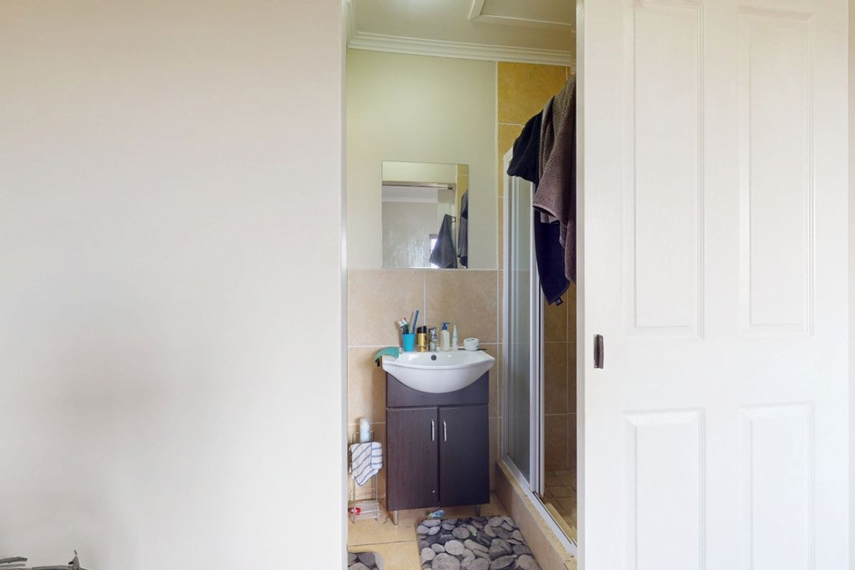 A compact bathroom featuring a vanity cabinet with a ceramic basin, a shower enclosure, and neutral wall tiling.